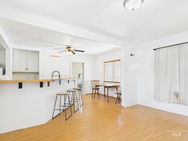 kitchen featuring a peninsula, a breakfast bar, ceiling fan, white cabinetry, and light wood finished floors