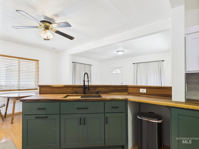 kitchen with a sink, light wood finished floors, wood counters, a ceiling fan, and green cabinets