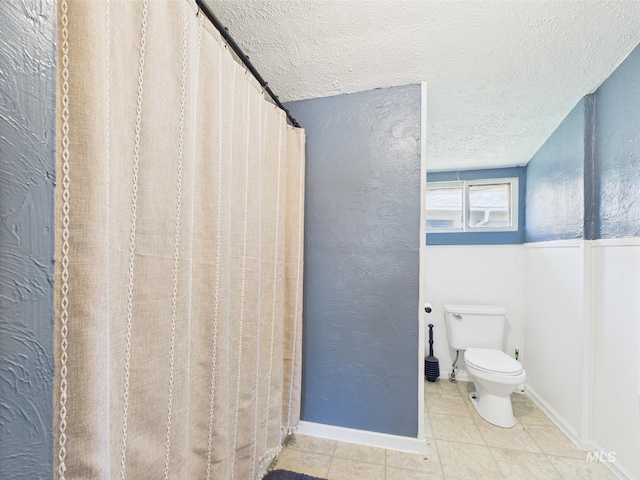 bathroom with toilet, a textured ceiling, baseboards, and tile patterned flooring