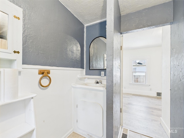 bathroom featuring vanity, a textured wall, a textured ceiling, and visible vents