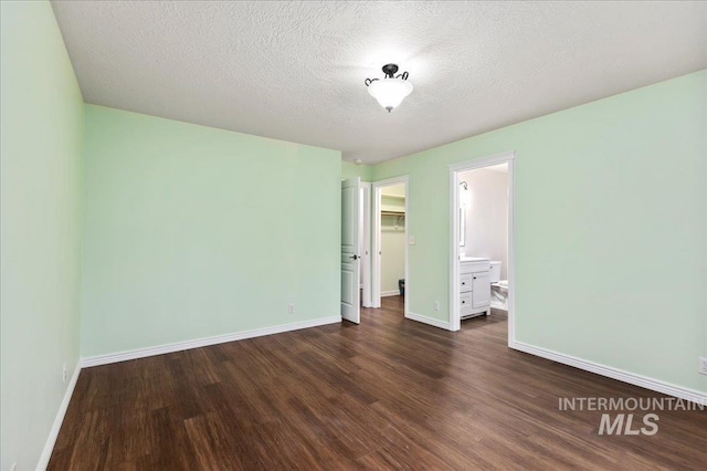 unfurnished bedroom with a closet, a spacious closet, a textured ceiling, ensuite bathroom, and dark hardwood / wood-style flooring