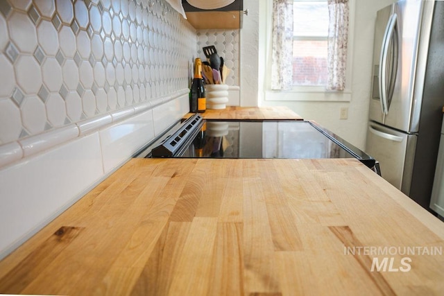 kitchen with black range, stainless steel refrigerator with ice dispenser, and tasteful backsplash