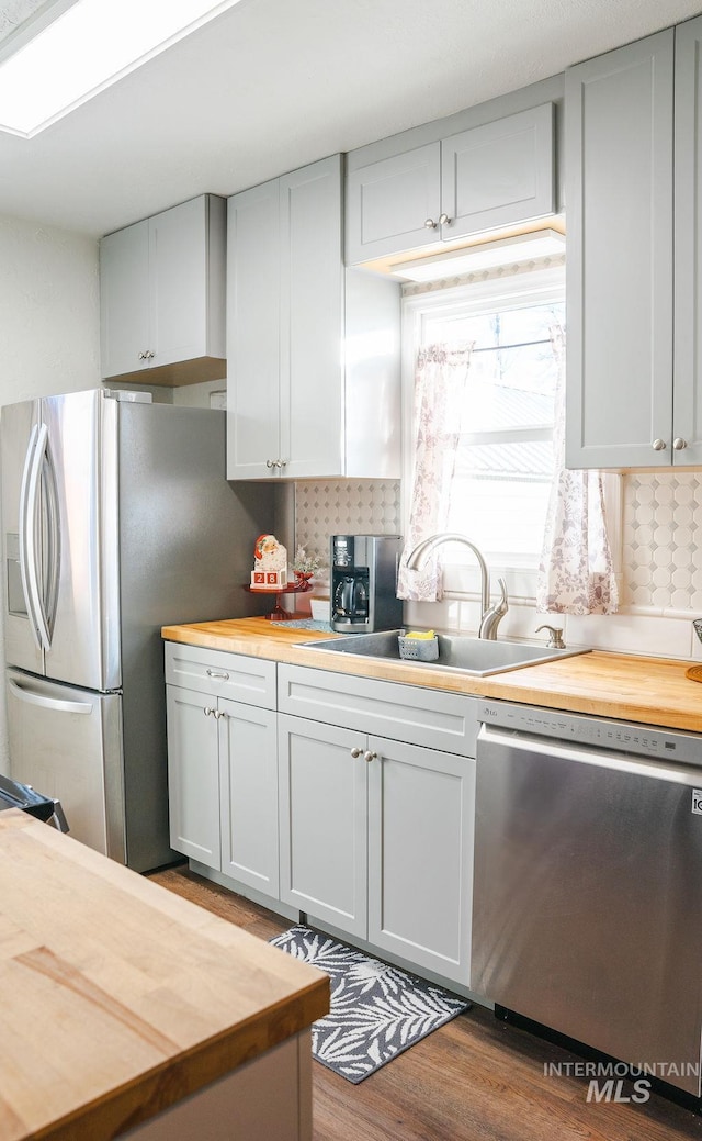 kitchen with wood counters, backsplash, sink, hardwood / wood-style flooring, and stainless steel appliances