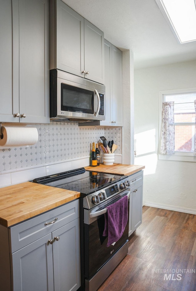 kitchen featuring dark hardwood / wood-style flooring, tasteful backsplash, appliances with stainless steel finishes, and wooden counters