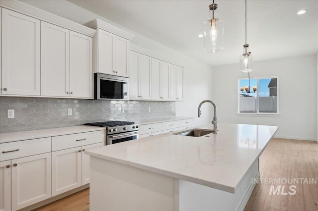 8828 S Waterclover Way, Meridian, ID 83642 - kitchen featuring stainless steel appliances, a sink, light wood finished floors, a kitchen island with sink, and tasteful backsplash