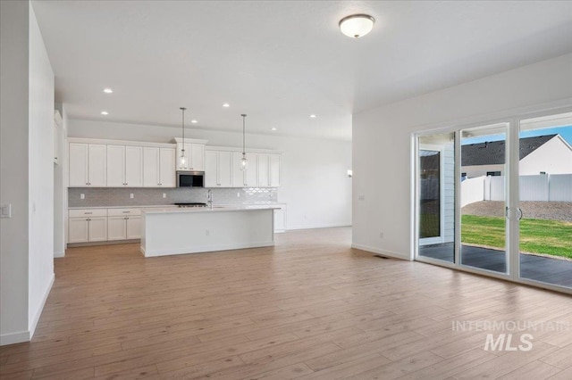8828 S Waterclover Way, Meridian, ID 83642 - kitchen with stainless steel microwave, light countertops, backsplash, light wood-style flooring, and recessed lighting