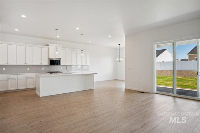 8828 S Waterclover Way, Meridian, ID 83642 - kitchen with stainless steel microwave, decorative backsplash, light countertops, light wood-style flooring, and a chandelier