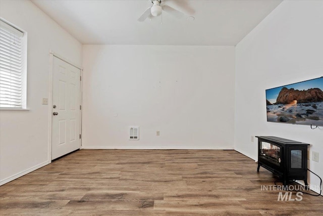 9740 W Shields Ave, Boise, ID 83714 - unfurnished living room featuring a wood stove, wood finished floors, a ceiling fan, and baseboards