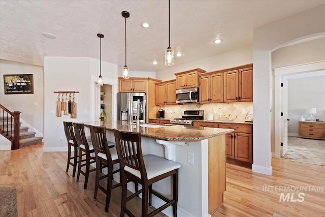 9740 W Shields Ave, Boise, ID 83714 - kitchen featuring appliances with stainless steel finishes, a sink, light wood-style floors, backsplash, and a breakfast bar