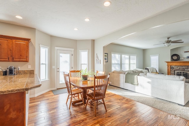 dining area featuring ceiling fan, a fireplace, light hardwood / wood-style floors, and a textured ceiling