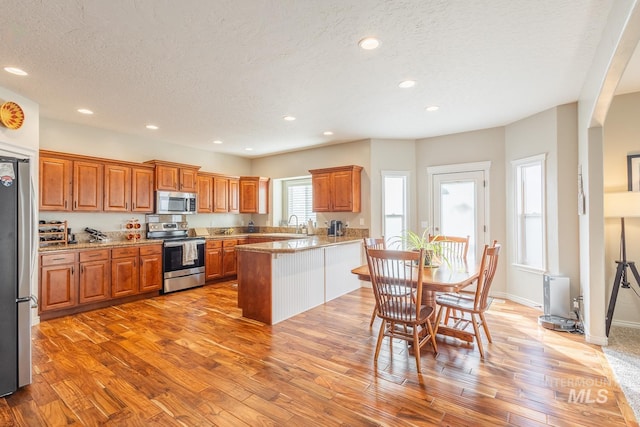 kitchen featuring stainless steel appliances, kitchen peninsula, a textured ceiling, and light wood-type flooring