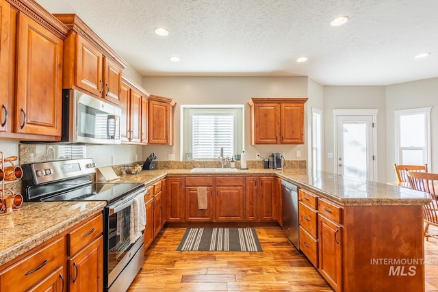 kitchen with sink, light hardwood / wood-style flooring, a textured ceiling, kitchen peninsula, and stainless steel appliances