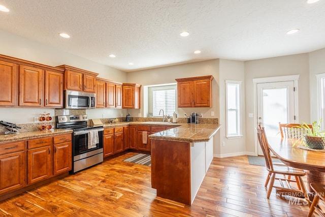 kitchen featuring appliances with stainless steel finishes, sink, kitchen peninsula, a textured ceiling, and light hardwood / wood-style flooring