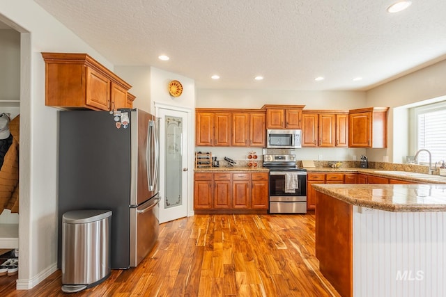 kitchen featuring stainless steel appliances, sink, a textured ceiling, and light wood-type flooring