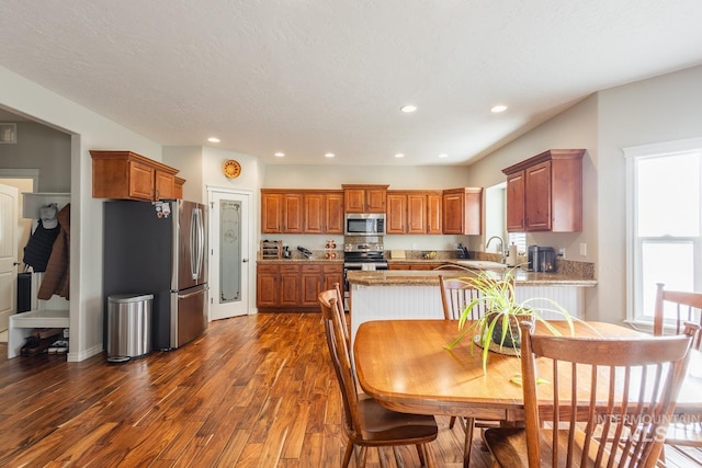 kitchen featuring appliances with stainless steel finishes, sink, light stone counters, kitchen peninsula, and dark wood-type flooring