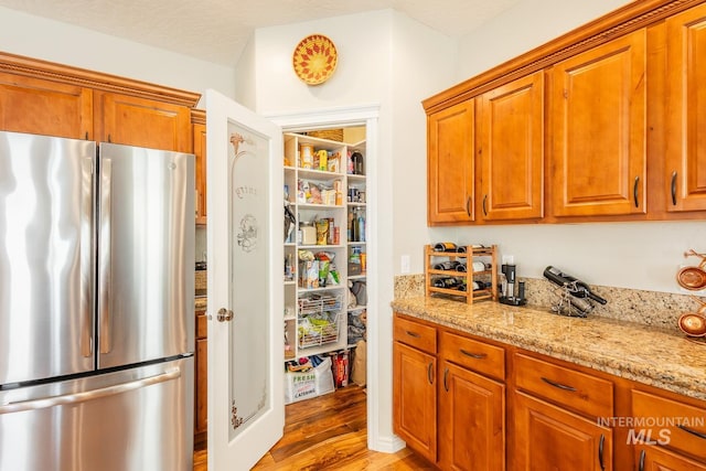 kitchen with light hardwood / wood-style floors, light stone countertops, and stainless steel refrigerator