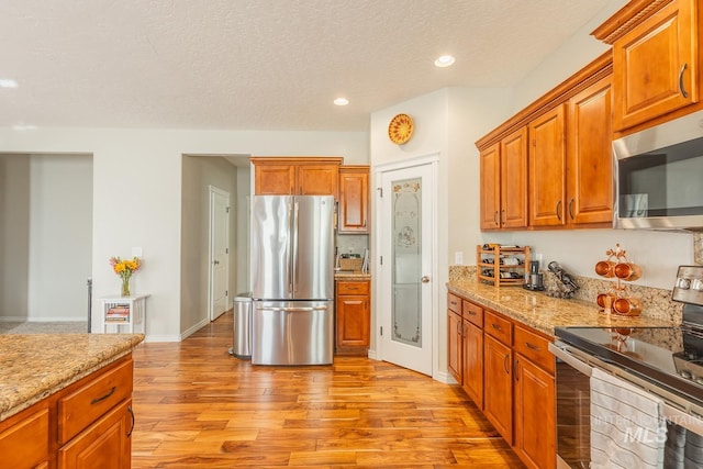 kitchen with stainless steel appliances, light stone countertops, light hardwood / wood-style flooring, and a textured ceiling