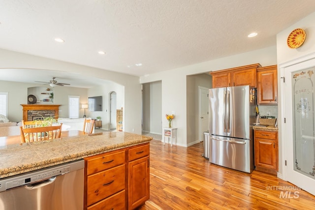 kitchen featuring a stone fireplace, a textured ceiling, ceiling fan, stainless steel appliances, and light hardwood / wood-style floors