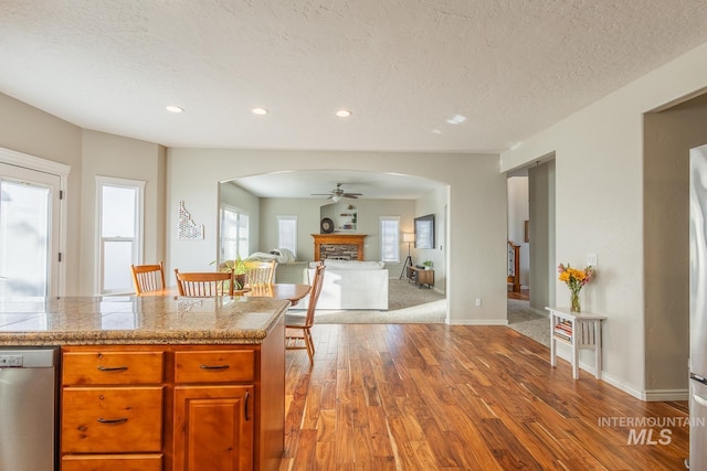 kitchen with a textured ceiling, light wood-type flooring, stainless steel dishwasher, ceiling fan, and a fireplace