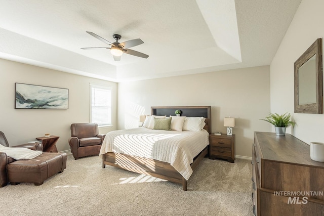 carpeted bedroom with ceiling fan and a tray ceiling