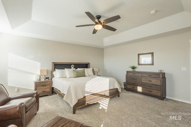 bedroom with ceiling fan, a tray ceiling, and light carpet