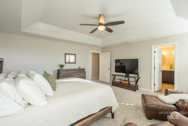 carpeted bedroom featuring ceiling fan, ensuite bathroom, and a raised ceiling