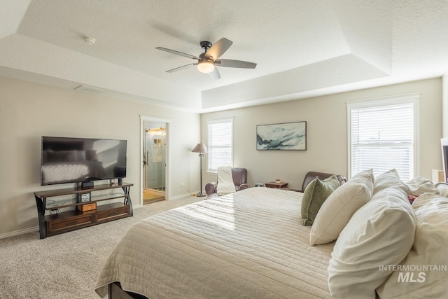 carpeted bedroom featuring ceiling fan, a tray ceiling, ensuite bath, and a textured ceiling