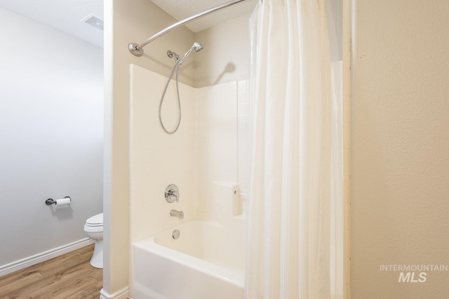 bathroom with hardwood / wood-style floors, shower / bath combo with shower curtain, and toilet