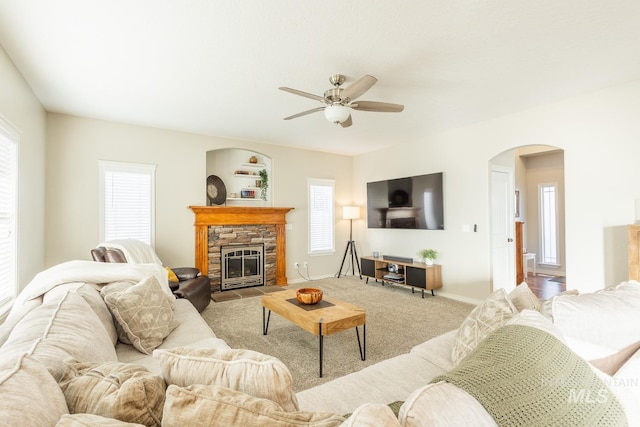 living room with a stone fireplace, a wealth of natural light, light colored carpet, and ceiling fan