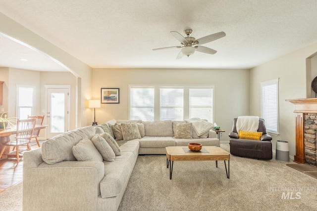 living room with ceiling fan, a fireplace, and a textured ceiling