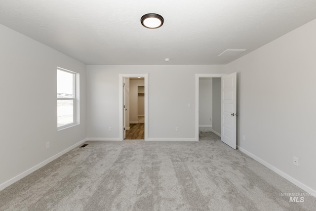 unfurnished bedroom featuring a walk in closet, light colored carpet, and a closet