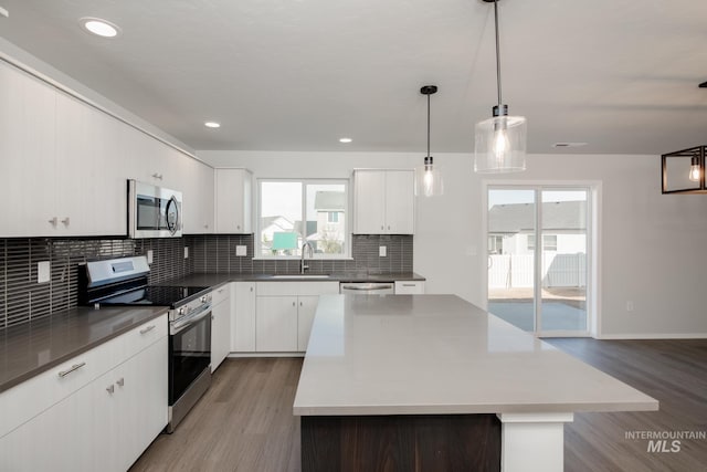 kitchen with appliances with stainless steel finishes, pendant lighting, white cabinetry, wood-type flooring, and a healthy amount of sunlight