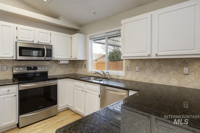 kitchen with white cabinets, vaulted ceiling, stainless steel appliances, and a sink