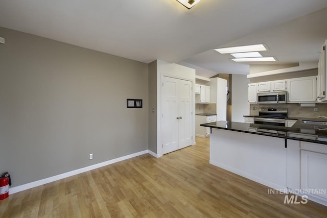 kitchen featuring vaulted ceiling with skylight, tasteful backsplash, dark countertops, a peninsula, and stainless steel appliances