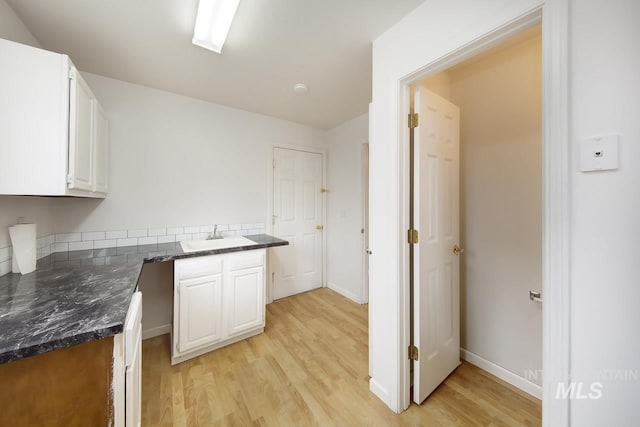 kitchen featuring light wood finished floors, baseboards, dark stone countertops, white cabinetry, and a sink