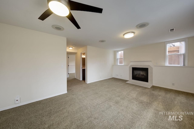 unfurnished living room featuring a healthy amount of sunlight, a fireplace with flush hearth, visible vents, and carpet flooring