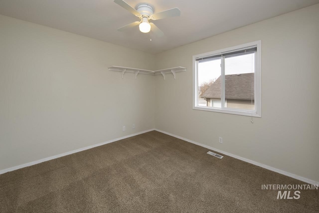 spare room with baseboards, visible vents, dark carpet, and a ceiling fan