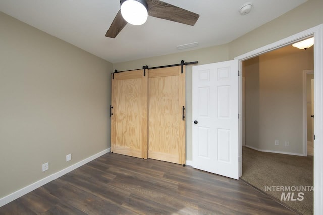 unfurnished bedroom featuring ceiling fan, baseboards, dark wood finished floors, and a barn door