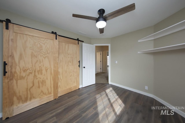 unfurnished bedroom with dark wood-style floors, a barn door, and baseboards