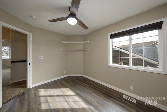 unfurnished room featuring dark wood-style flooring, visible vents, ceiling fan, and baseboards