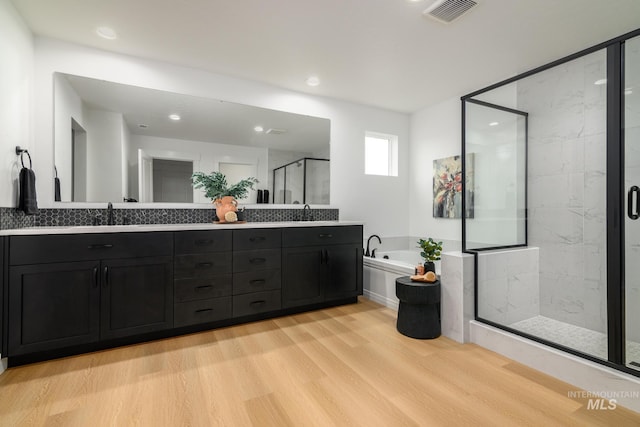 bathroom featuring double vanity, a stall shower, visible vents, wood finished floors, and a garden tub