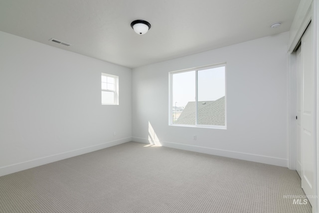 spare room with light carpet, visible vents, and baseboards