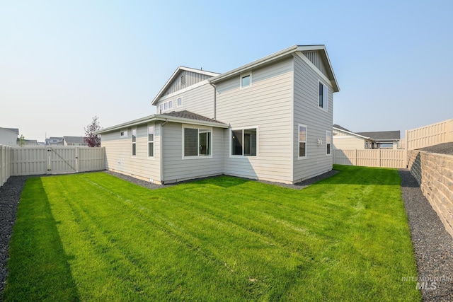 back of property featuring a yard, board and batten siding, a fenced backyard, and a gate