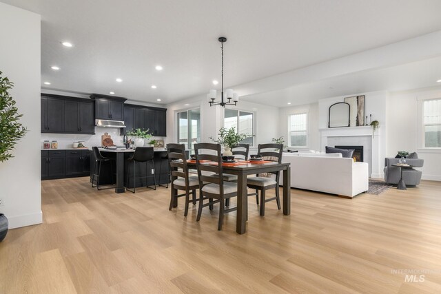 dining area featuring baseboards, a glass covered fireplace, light wood-style flooring, and recessed lighting