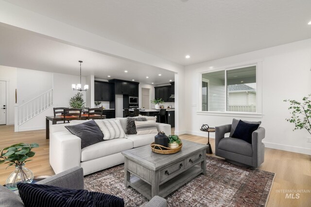 living room featuring a chandelier, light wood-style flooring, baseboards, and stairs