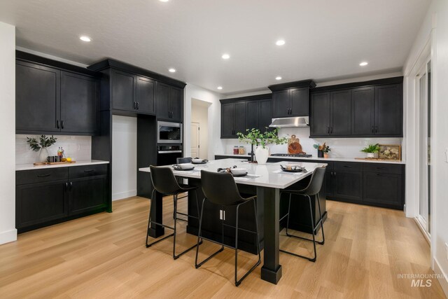 kitchen with dark cabinets, under cabinet range hood, light wood-style floors, light countertops, and appliances with stainless steel finishes