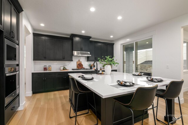 kitchen featuring dark cabinets, under cabinet range hood, a sink, light countertops, and light wood finished floors