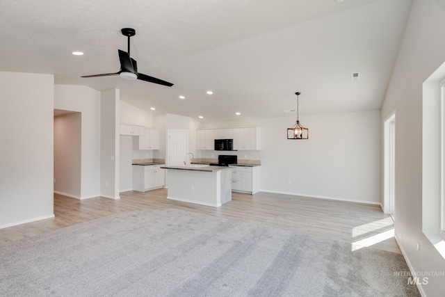 kitchen with a kitchen island with sink, white cabinets, vaulted ceiling, and light carpet