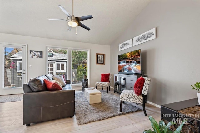 living room with baseboards, light wood finished floors, lofted ceiling, ceiling fan, and a textured ceiling