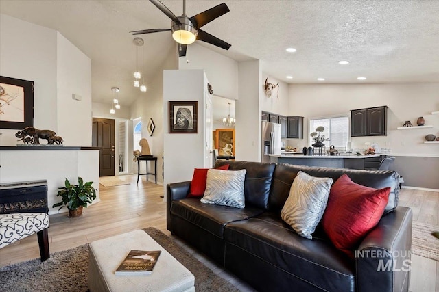 living area with high vaulted ceiling, ceiling fan with notable chandelier, a textured ceiling, recessed lighting, and light wood finished floors